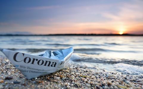 Papierschif aus Zeitzúng gefaltet hat den Aufdruck "Corona" und liegt am Strand