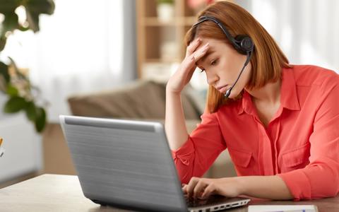 Frau mit Headset am Laptop fasst sich gestresst an die Stirn