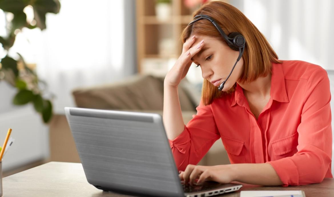 Frau mit Headset am Laptop fasst sich gestresst an die Stirn