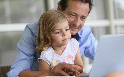 Vater sitzt mit Tochter auf dem Schoß vor einem Laptop