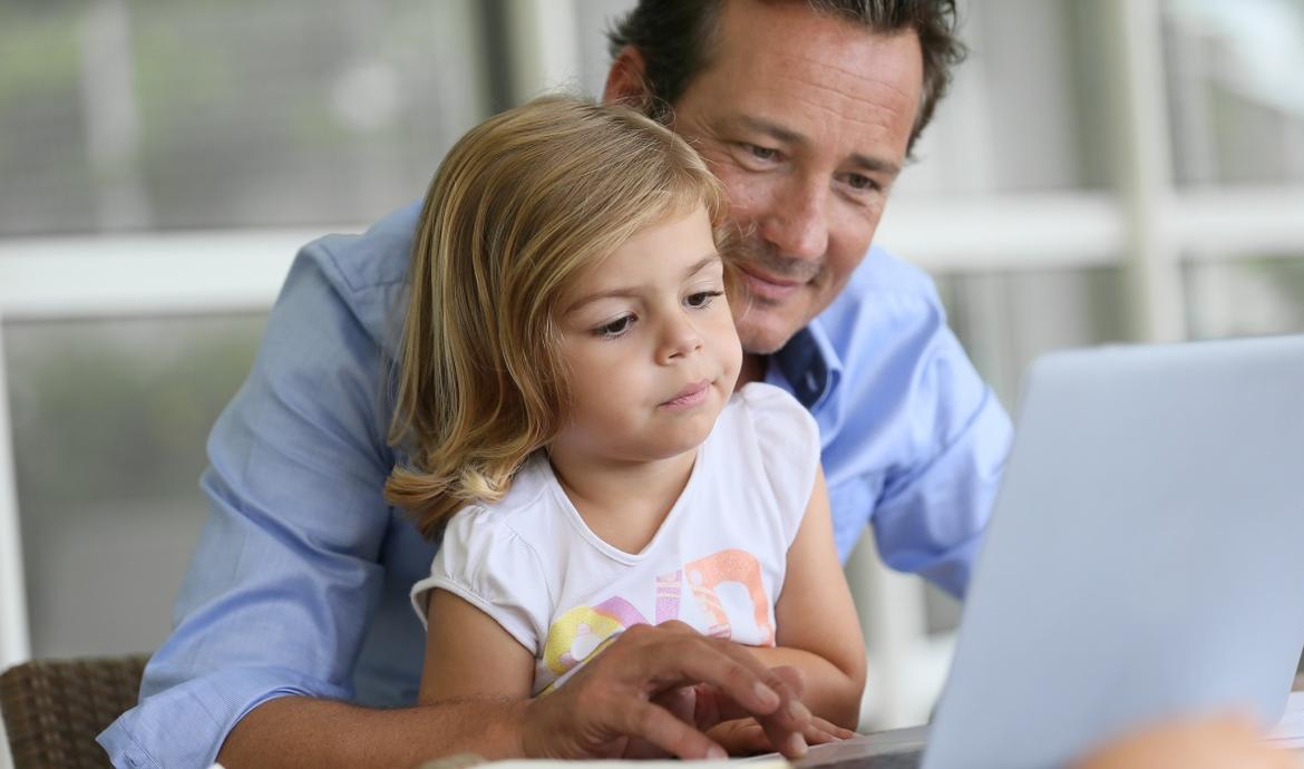 Vater sitzt mit Tochter auf dem Schoß vor einem Laptop