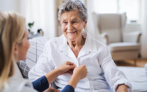 Pflegekraft hilft alter Frau beim Anziehen einer Bluse